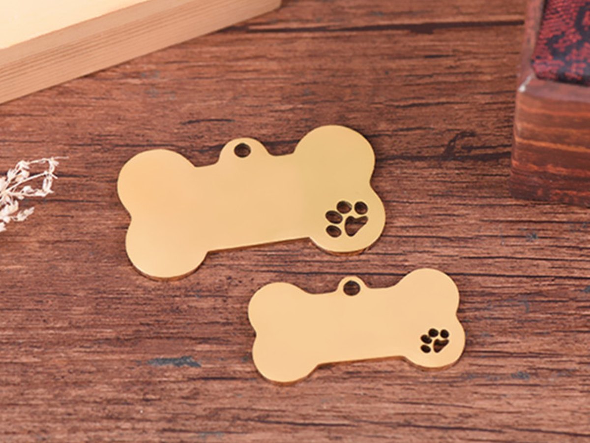 Brushed brass bone shaped pet tag engraved with a paw print, standing on a wooden table